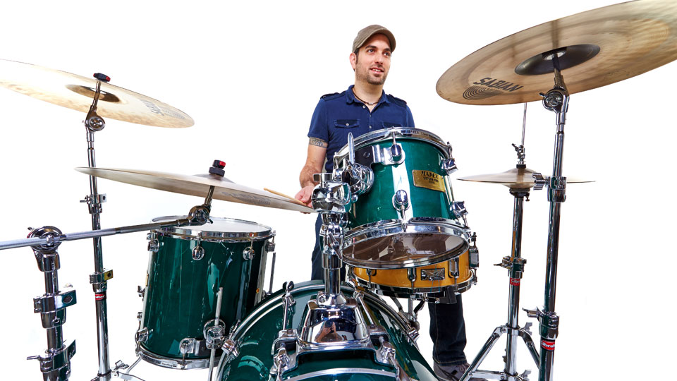 Portfolio image: professional photograph of B.J. Capelli seated at a shiny turquoise drum kit, smiling and optimistically looking up and ahead.